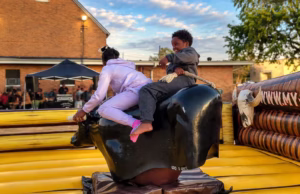 Children taking turns riding a Mechanical Bull at an outdoor event.