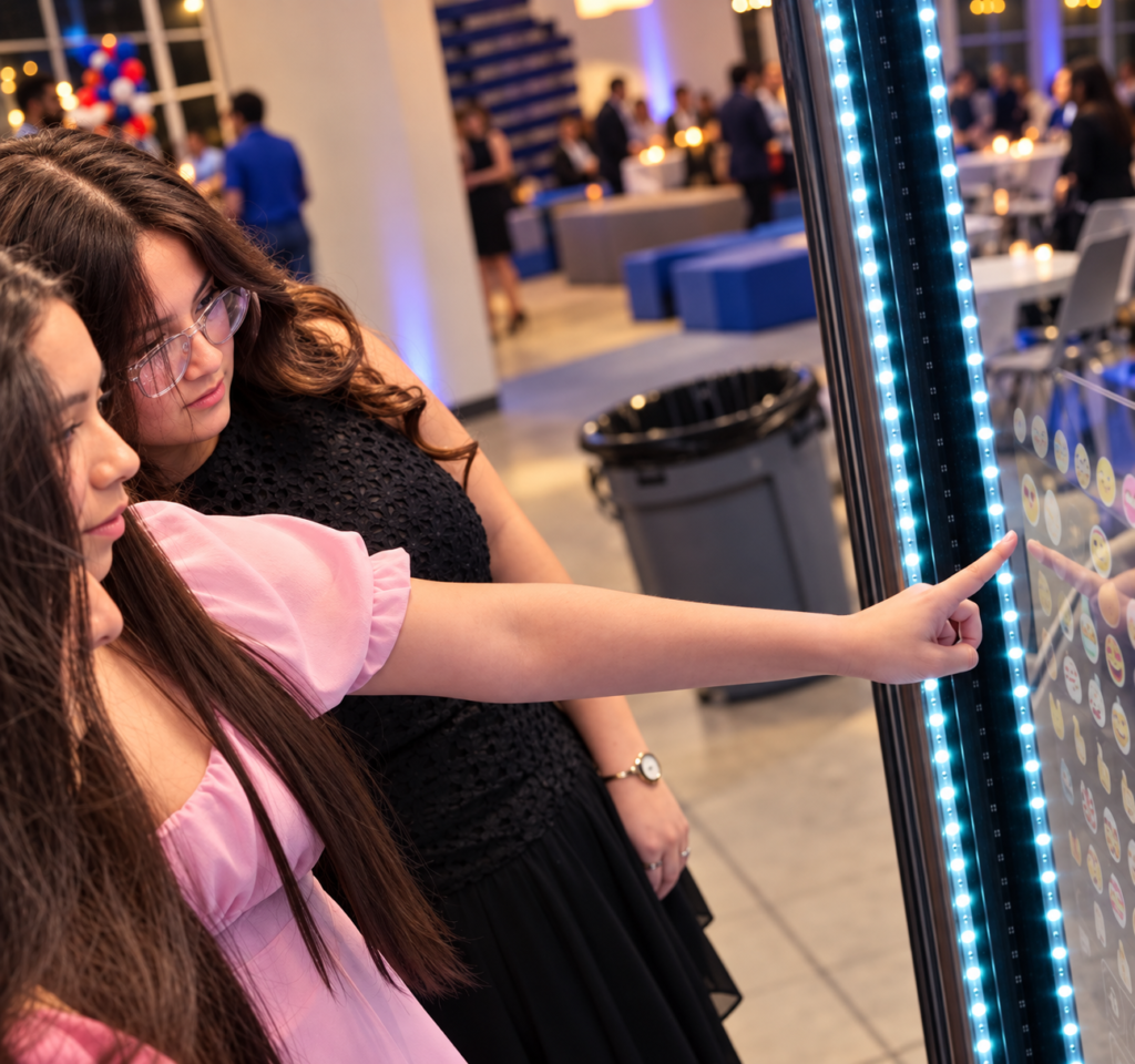 Guests using an interactive photo booth with LED lights at an indoor event, touching the screen to select digital effects and capture fun memories.
